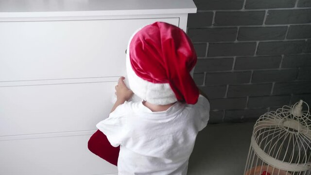 Little baby boy putting gift into Christmas sock hanging on commode at home