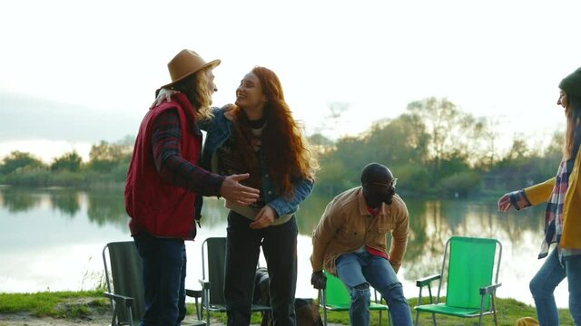 Stylish hipster friends met eath other sitting near lake. Four young people hug smiling with dog. Vacation tourism adventure outdoors. Close up. Slow motion