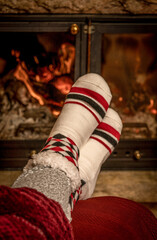 Fototapeta na wymiar Winter night, happy woman resting by the fire with her feet in wool socks. Cozy scene.