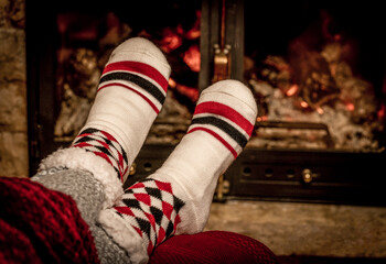 Fototapeta na wymiar Winter night, happy woman resting by the fire with her feet in wool socks. Cozy scene.