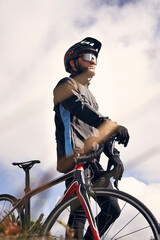 Prefessional male cyclist in sportswear, glasses and protective helmet walking with his bike in the forest to take a break after riding
