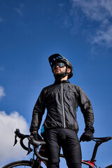 Beautiful portrait of a cyclist at sunset, young man rides a modern carbon fiber mountain bike in sportswear. Portrait of a men in a helmet, glasses and windbreaker jacket. 