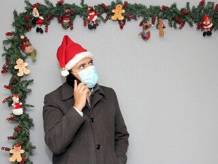 
Latin man with protection mask, coat and Santa Claus hat in video call with cell phone and...