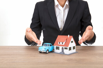 A small house and a model car are placed on the table. Female hands in formal wear at the table make an introduction.