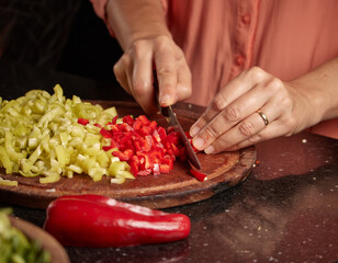 Closeup shot of a woman chopping peppers on a wooden board