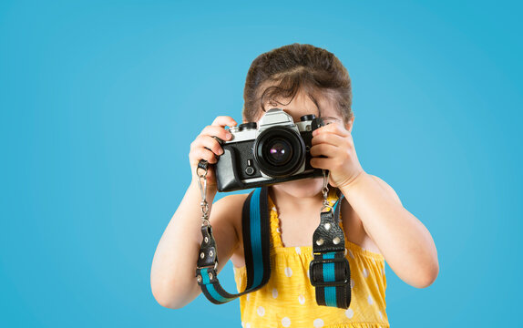 Little girl photographer in yellow dress taking picture with film camera isolated on blue background