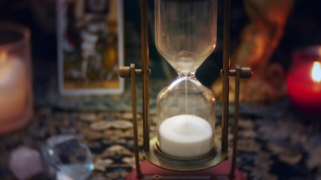 The sands of time pass by in the hourglass. The sandglass reflects light from candles.  When sand timer runs out, a death tarot card is revealed symbolizing the end of life.
