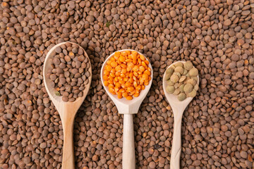 dry orange, red, green lentils in wooden spoons on a black background top view, flat lay
