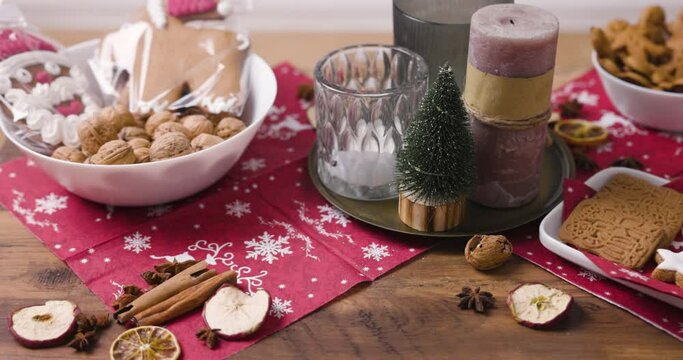 beautifully decorated christmas table with candles, christmas cookies, nuts, gingerbread, dried fruits, cinnamon stars and cinnamon sticks and a christmas tree in background in 4k