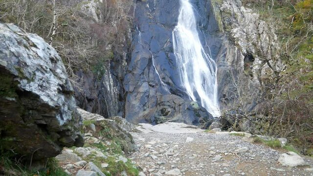 Rocky cascading waterfall flowing into jagged river rocks dolly left to boulder