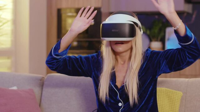 Happy woman at home experiencing virtual reality 3D games simulation entertainment activity wearing VR headset helmet in living room. Technologies concept.