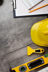 Fototapeta premium Contractor concept. Tool kit of the contractor: yellow hardhat, libella, hand saw. Plans and notebook on the gray tiles background.