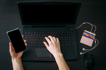 Top view woman's hand holding smartphone, laptop computer with blank screen on black background. Using gadgets for business, searching information in workplace at home office.