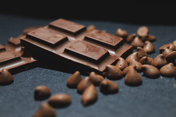 close up of dark chocolate bar and chocolate drops in a dark background.