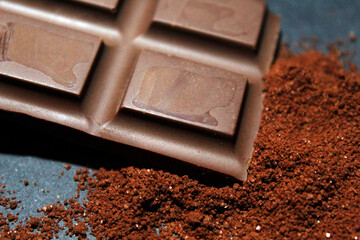 Close up of chocolate bar with chocolate powder in a black background.