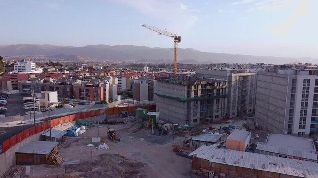 Drone flying over an incomplete construction where you can see the crane, tractor, workers and a car park.