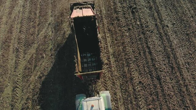 Aerial view of a modern tractor with a trailer manure spreader in the autumn field. An agricultural machine applies organic fertilizers to brown soil to increase future yields and farmland fertility