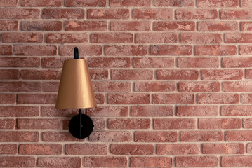 Stylish small golden lamp sconce installed on red brick wall against brown window curtain in contemporary apartment room closeup. Interior design details.