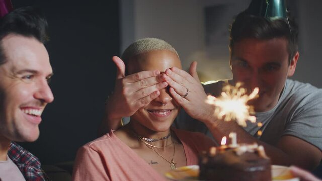 Group of friends meeting to celebrate womans birthday at home covering her eyes and surprising her with cake - shot in slow motion