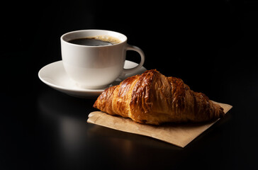 A croissant and hot coffee on a black background