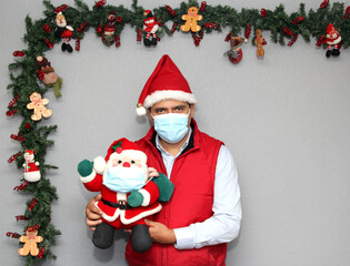 latin man with protection mask and santa claus doll in christmas decoration, new normal covid-19