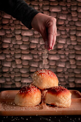 bread buns with sesame on wooden plate dark table brick wall, with the chef's hand adding the sesame