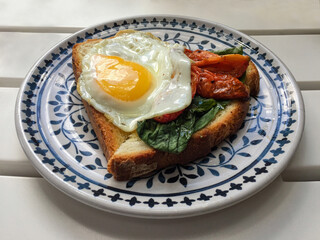 Breakfast served with toast, a sunny side up egg, sun dried tomatoes and basil