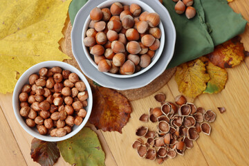 Whole hazenuts in a bowl with cracked hazenuts and autumnal leaves on wooden background