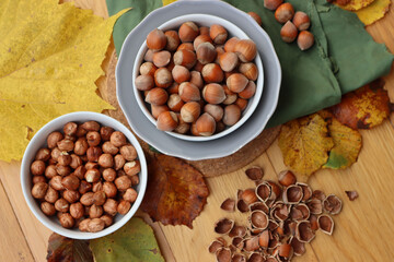 Whole hazenuts in a bowl with cracked hazenuts and autumnal leaves on wooden background