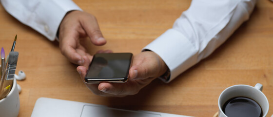 Male hands holding smartphone on wooden worktable
