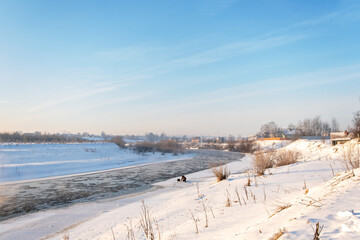 Winter snow river landscape. Rural scene. Ice floats on the river. Steam escaping over the frozen river in winter
