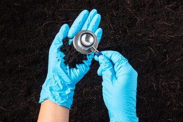 Hand of researcher woman wear gloves holding a stethoscope on fertile black soil for check...