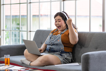  fat asian female wearing casual cloth with headphones sitting on a couch feeling happy and hail...