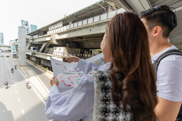 Couple travelers holding a paper map in hands together and looking and finding destination and station for lines of a sky train in a big city. Idea for tourists travels on vacation