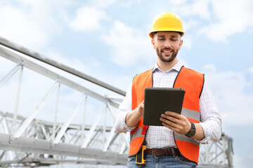 Professional engineer with tablet near high voltage tower construction outdoors. Installation of...