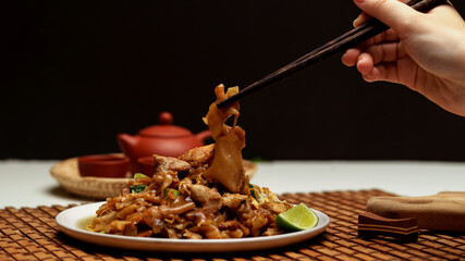 Obraz na płótnie Canvas Female hand holding chopstick to eat Stir fried Noodle with sweet soy sauce (Pad See Ew)