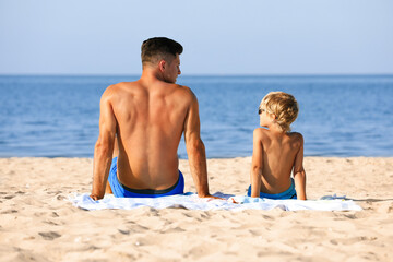 Father and son on sandy beach near sea. Summer holidays with family