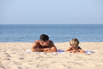 Fototapeta na wymiar Father and son lying on sandy beach near sea. Summer holidays with family