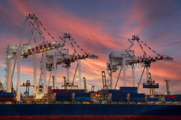 View of container cargo ship and crane bridge in shipyard at sunrise