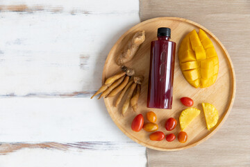 healthy organic drink from ginger fingerroot pineapple tomato and mango in a plastic bottle in a wooden tray on rustic fabric table. Concept of natural drink for immunity boosting, detox, and diet