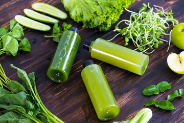 various vegetable ingredients place around bottles of green healthy juice on an antique wooden table from top view. Lifestyle, diet, detox, body cleansing food concept