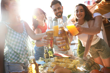 Happy friends toasting with beer and juice outdoors at table. Camping season