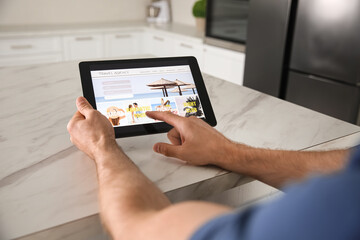 Man booking tickets online on tablet at table, closeup. Travel agency concept