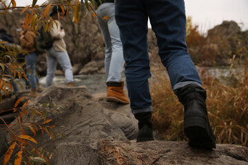 Group of friends crossing mountain river, focus on hiking boots