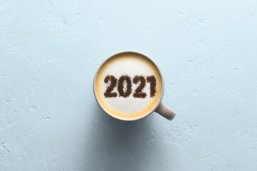 New year background. Number 2021 on frothy surface of cappuccino in coffee cup on pastel blue background. Food creative concept. Top view, copy space