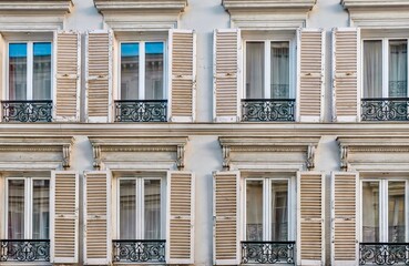 Close-up view of traditional French windows with open wooden shutters and elegant wrought iron...