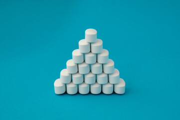 pharmacology medical concept pyramid of white pills tablets drugs on cyan surface with copyspace