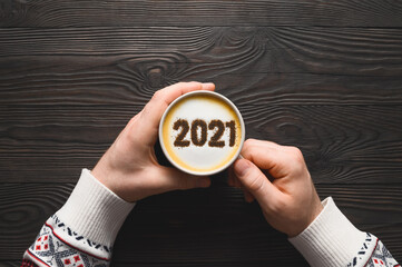 New year background. Male hands hold coffee cup with number 2021 on frothy surface of cappuccino....