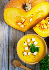 Pumpkin and carrot soup, tadka with cream and parsley on dark wooden background. Top view