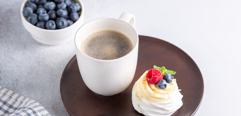 Romantic spring breakfast. Delicious Pavlova cake with cream and fresh berries and mug with coffee. Soft focus